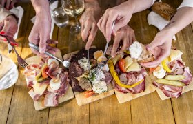Heurigenjause, © Weinviertel Tourismus GmbH / Herbst Mehrere Hände greifen nach Aufschnitt und Käse auf Holzplatten.