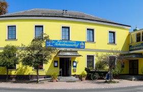 Auland-Hotel Siebenbrunnerhof, © Auland-Hotel Siebenbrunnerhof Gelbes Gebäude mit Restaurant und Hotel, umgeben von Bäumen und Straße.