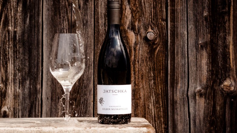 Weingut Jatschka, © Astrid Bartl Eine Weinflasche und ein Glas mit Wasser vor einer Holzwand.