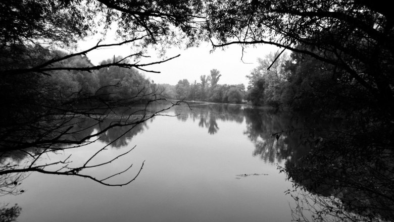 March meadows, © Weingut Zirnsack Black and white photo of a calm river surrounded by trees.
