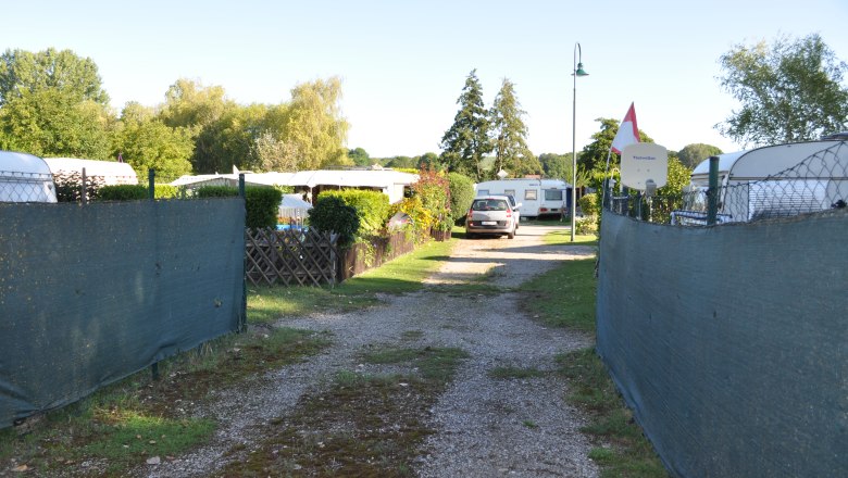 Campingplatz am Badeteich, © Weinviertel Tourismus Ein Campingplatz mit Wohnwagen und einem Auto auf einem Schotterweg, umgeben von Bäumen und Zäunen.