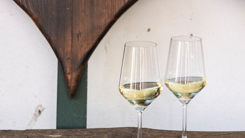 Wine glasses, © Weinviertel Tourismus / Doris Schwarz-König Two wine glasses with white wine on a rustic wooden table in front of a heart-shaped wooden decoration.