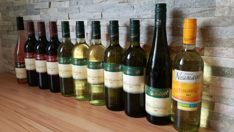 Weinsortiment, © Weingut Neumayer Eine Reihe von Weinflaschen des Weinguts Neumayer vor einer Steinwand.