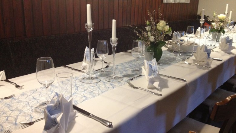 Table setting, © Fam. Haselbauer Elegant, festively laid table with white tablecloths, candles and flower arrangements.