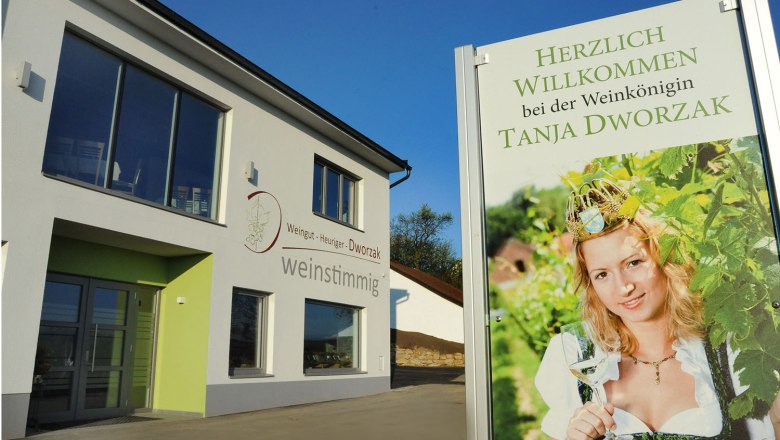 Welcome to the Wine Queen, © Herbert Schleich A modern building with a sign showing a woman in traditional costume with a wine glass. Text: Welcome to the wine queen Tanja Dworzak.
