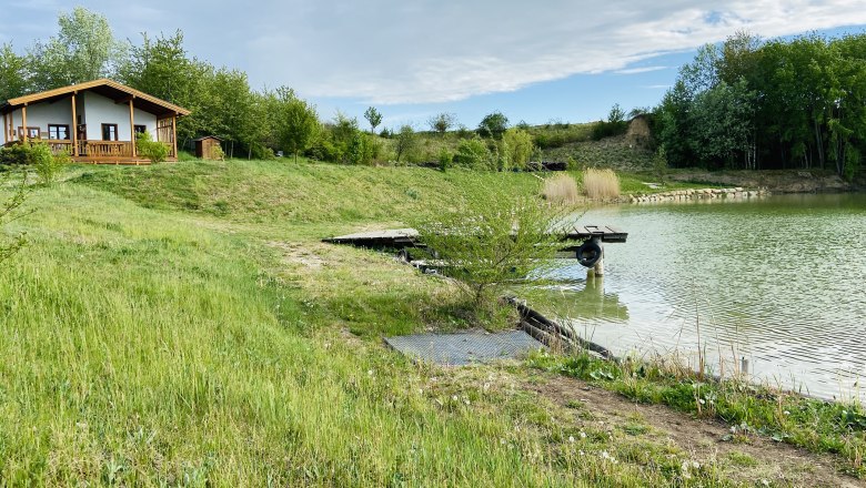 Old brick kiln pond, © Weinstraße Weinviertel A small house on the banks of a pond with a green meadow and trees in the background.