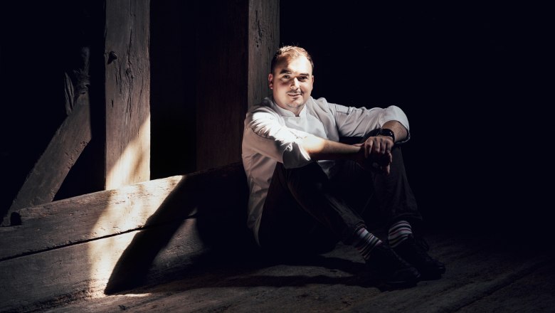 In der Küche von Samuel Pope trifft Weinviertel auf England, © Niederösterreich Werbung/Julius Hirtzberger Mann in weißem Hemd sitzt im Schatten auf Holzboden.