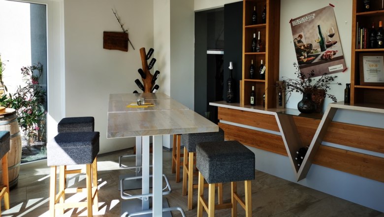 Tasting room, © Weinstraße Weinviertel Modern tasting room with wooden table, bar stools and wine racks.