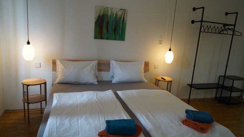 Landhaus Krell, © Weingut Krell Modernes Schlafzimmer mit Doppelbett, zwei Nachttischen, Hängelampen und Handtüchern auf dem Bett.