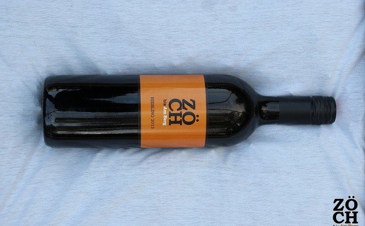 Zöch Wein, © Fam. Zöch Eine Weinflasche mit orangefarbenem Etikett der Marke Zöch auf einem hellen Hintergrund.