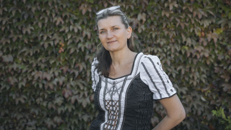 Wirtin Elzbieta Burgstaller, © Niederösterreich Werbung/David Schreiber Frau in traditioneller Kleidung vor einer mit Efeu bewachsenen Wand.