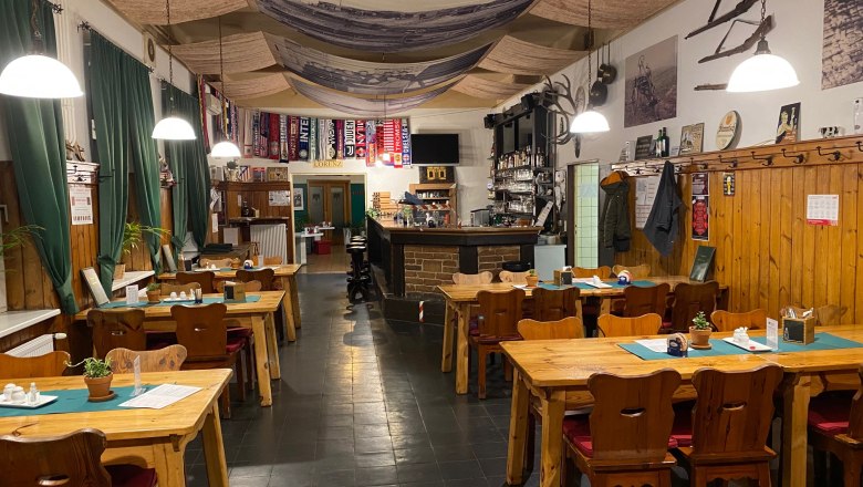 Restaurant, © Andreas Sinnhuber Cozy dining room with wooden tables, chairs and bar, decorated with soccer scarves and rustic elements.