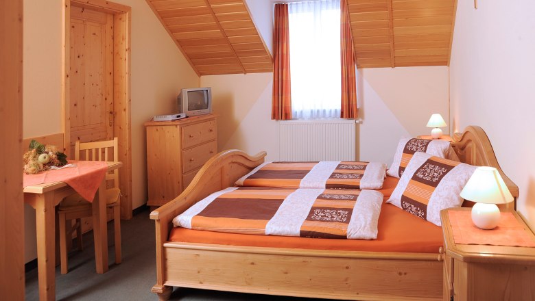 Guest room, © Seher Cozy guest room with wooden furniture, double bed, small table, TV and sloping ceiling.