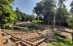 Motorikpark Hollabrunn, © Stadtgemeinde Hollabrunn Ein Motorikpark mit verschiedenen Holzelementen und Klettergeräten, umgeben von Bäumen und Grünflächen.