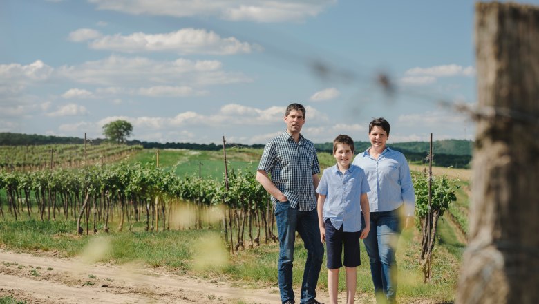 Herzlich Willkommen, © Michael Reidinger Eine Familie steht in einem Weinberg unter blauem Himmel.