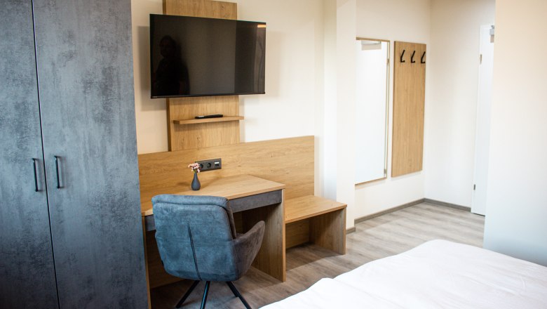 Geräumige Zimmer, © Bärenhof Modern eingerichtetes Hotelzimmer mit Schreibtisch, Fernseher, Kleiderschrank und Spiegel.