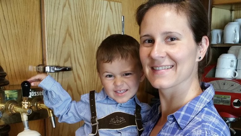 Klapka family, © Gasthaus Klapka A woman holds a child in lederhosen by a beer tap. Bottles of spirits can be seen in the background.