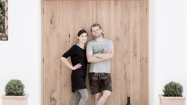 Bio-Weinbau Weber, © Familie Weber Zwei Personen stehen vor einer Holztür, daneben eine große Weinflasche und Pflanzen in Töpfen.