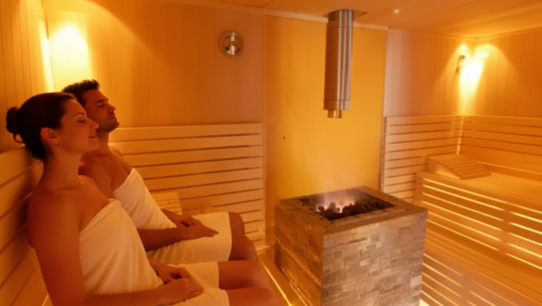 Sauna, © Austria-Best-Hotels Zwei Personen entspannen in einer Sauna mit Holzbänken und einem Ofen in der Mitte.