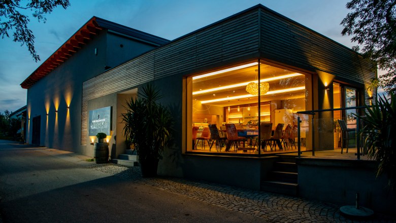 Weinkeller Weingut Hebenstreit, © Martin Lifka Photography Modernes Gebäude mit Glasfront und Innenbeleuchtung bei Dämmerung.