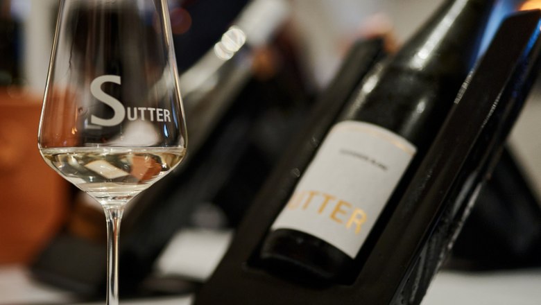 Weingut Sutter, © Martin Mathes Ein Weinglas mit der Aufschrift 'Sutter' steht vor einer Weinflasche auf einem Tisch.