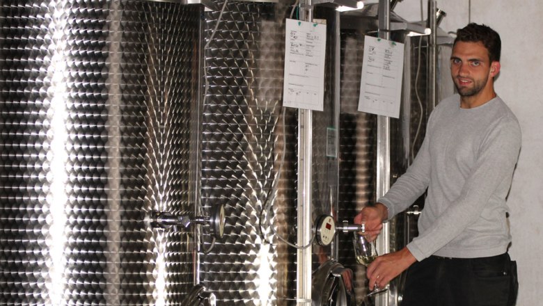 In the wine cellar, © Familie Fein A man draws wine from a stainless steel tank in a wine cellar.
