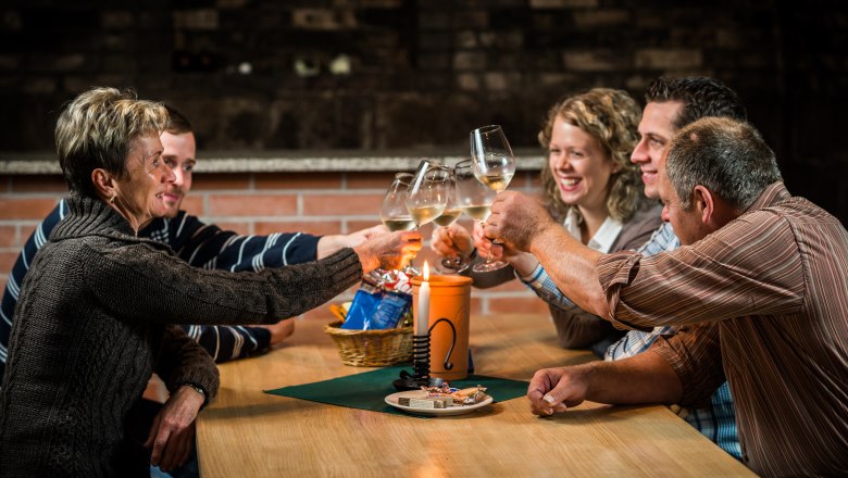 Ein Achterl in Ehren, © Marek Knopp Fünf Personen stoßen mit Weingläsern an einem Tisch an.