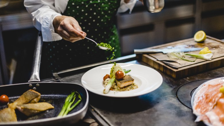 Die Küche: Bodenständig saisonal, © Niederösterreich Werbung/David Schreiber Koch dekoriert ein Gericht mit Kräutern in einer Küche.