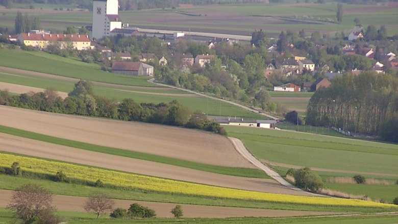 Großmugl, © Gemeinde Großmugl Landschaft mit Feldern und einem Dorf im Hintergrund, dominiert von einem großen weißen Gebäude mit dunklem Dach.