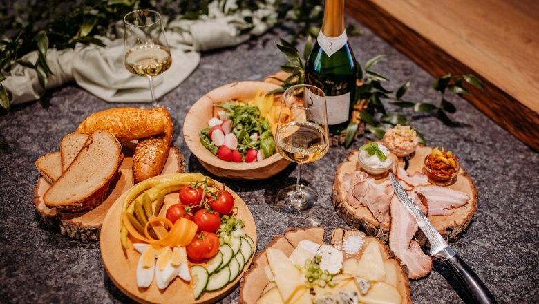 Heurigen snack, © Claudia Müllner Various dishes on wooden plates with wine bottles and glasses.