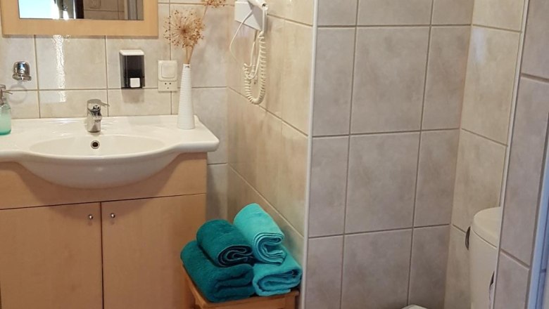 Badezimmer, © Sabine Wambach Ein Badezimmer mit Waschbecken, Spiegel, Toilette und Handtüchern auf einem Hocker.