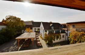 Weingut, © Zuschmann-Schöfmann Innenhof eines Weinguts mit Holzbauten und Weinreben.