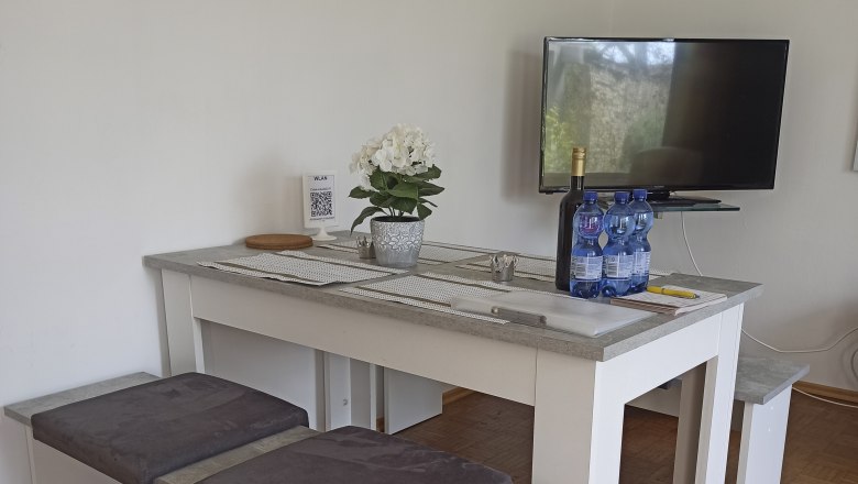 Aufenthaltsbereich, © Multimedia Lauda Moderner Aufenthaltsbereich mit Tisch, Bänken, Fernseher und Dekoration.