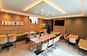 Moderner Verkostungsraum, © Weingut Schwinner Moderner Verkostungsraum mit Holztischen, gepolsterten Stühlen und dekorativen Regalen mit Flaschen.