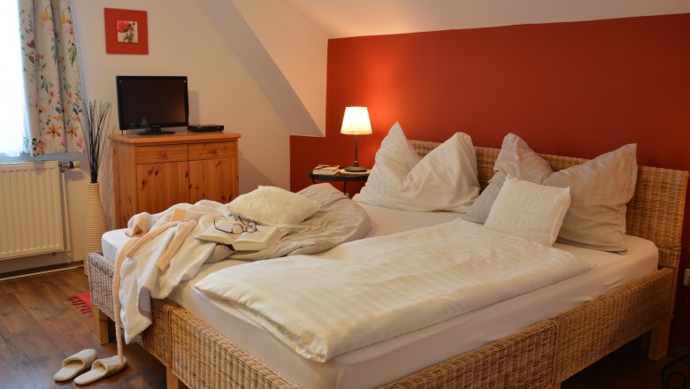 Doppelzimmer, © Christine Nigl Gemütliches Doppelzimmer mit roter Wand, Bett, Nachttischlampe, Fernseher und Holzmöbeln.