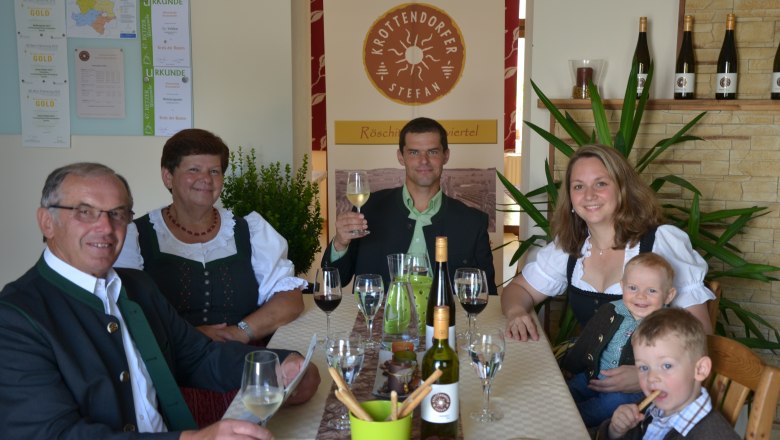 Familie Krottendorfer, © Familie Krottendorfer Familie in traditioneller Kleidung sitzt an einem Tisch mit Wein und Gläsern.