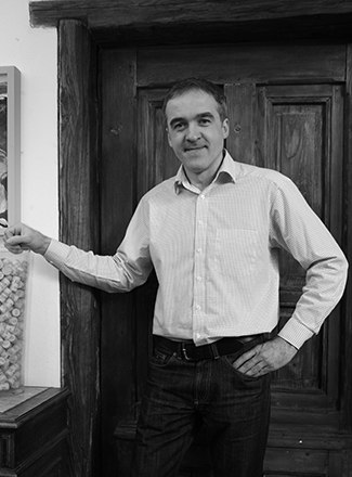 Winzer, © Roman Bayer Ein Mann in einem Hemd steht vor einer Holztür und lächelt in die Kamera.