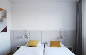 Gästezimmer, © Stadthotel Hollabrunn Modernes Gästezimmer mit zwei Einzelbetten, gelben Kissen und Wandlampen.