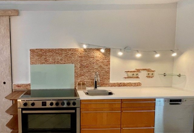 Küche, © Julia Grünschachner Moderne Küche mit Herd, Spüle und Geschirrspüler vor einer Mosaikfliesenwand.