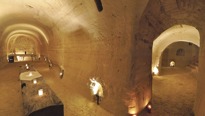 Sky cellar, © Himmelkeller Underground sandstone cellar with candlelight and rustic tables.