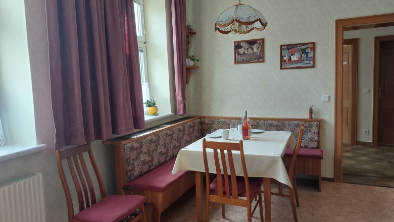 Eat-in kitchen, © Erika Kellner Cozy eat-in kitchen with dining table, chairs and corner bench. Window with curtains, pictures on the wall.