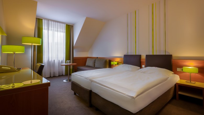 City Hotel Doppelzimmer, © © Markus Jung, MJM Photography Modernes Hotelzimmer mit zwei Einzelbetten, grünen Lampen und einem Schreibtisch. Fenster mit Vorhängen im Hintergrund.