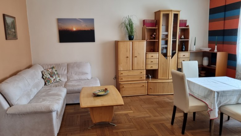 Haus Waschbergblick, © Wolfgang Greil Wohnzimmer mit beiger Couch, Holzmöbeln und Esstisch.