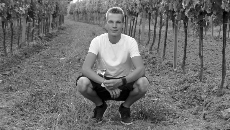 Roman Wagner, © Weingut Wagner Person hockt in einem Weinberg mit einem Weinglas in der Hand.