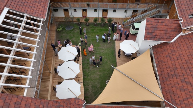 Wonderful ambience in the inner courtyard, © Felix Korfmann Bird's eye view of the inner courtyard with green lawn, white parasols and guests at a reception.