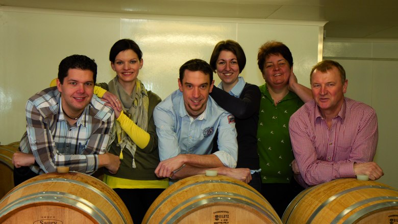 Familie Mauser, © Martin Mauser Sechs Personen lehnen sich auf Weinfässer in einem Keller.