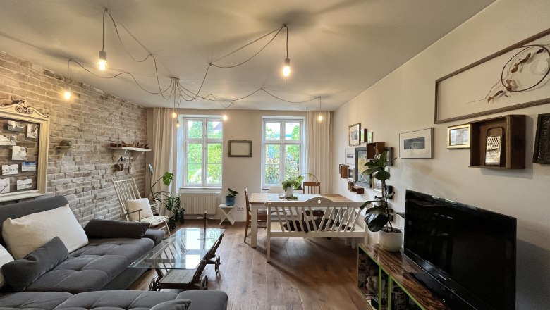 Wohnraum, © Elisabeth Fürlinger Gemütliches Wohnzimmer mit grauem Sofa, Holztisch, Pflanzen und Wanddekorationen.