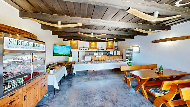 Spritzerrast – Campingstellplatz mit Jause und Panoramablick, © Bernhard Raab Innenansicht eines rustikalen Gastraums mit Holzmöbeln und einem Kühlschrank voller Getränke.