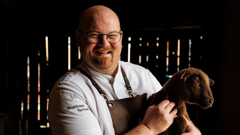 Herbst Inn, © Weinviertel Tourismus / Michael Reidinger A man in chef's clothes holds a brown sheep in a stable.