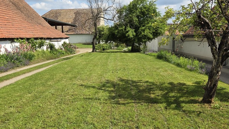 Motorhome parking space, © Fam. Krottendorfer Green meadow with trees and buildings in the background under a blue sky with clouds.